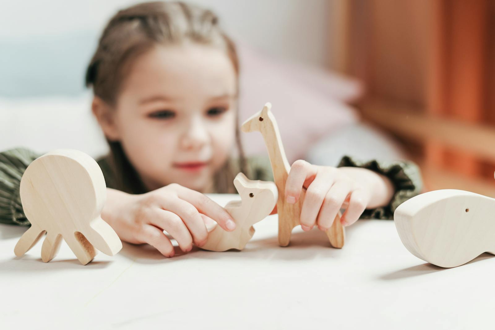 Young girl engages creatively with wooden animal toys in a playroom setting.